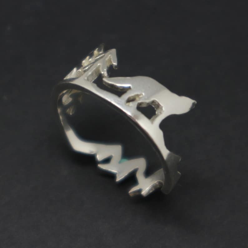 May include: A silver ring featuring a cut-out design of a mountain range and a wolf howling at the moon.