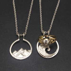 May include: Two silver necklaces with matching pendants. One pendant features a mountain range design, while the other features a wave design. The wave pendant also has a gold ring with a clear stone.