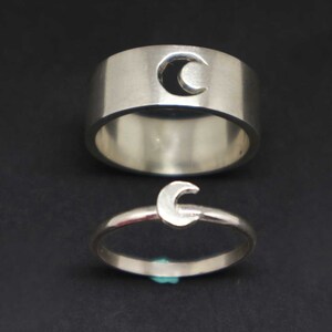 May include: Two silver rings with a crescent moon design. The larger ring has a cut-out crescent moon, while the smaller ring has a solid crescent moon.