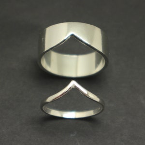 Könnte beinhalten: Zwei silberne Ringe mit einem V-förmigen Ausschnitt. Der größere Ring ist breiter und hat eine ausgeprägtere V-Form.