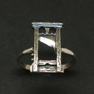 May include: A silver ring featuring a guillotine design. The ring is crafted from metal and has a detailed design.
