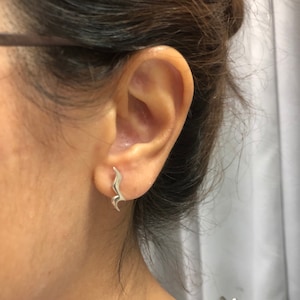 Op de afbeelding: Een close-up van iemands oor met een zilveren oorring in de vorm van een vioolsleutel.