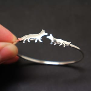 Puede incluir: Pulsera de plata con dos siluetas de zorros, una más grande que la otra, que se miran.