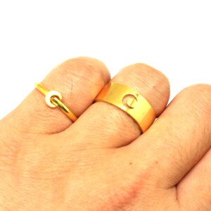 May include: Two gold rings on a hand. The larger ring has a cut-out letter "C" and the smaller ring is a simple band with a crescent moon shape.