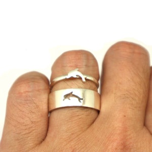 May include: Two silver rings with dolphin designs. The top ring has a dolphin cutout, and the bottom ring has a solid dolphin design.