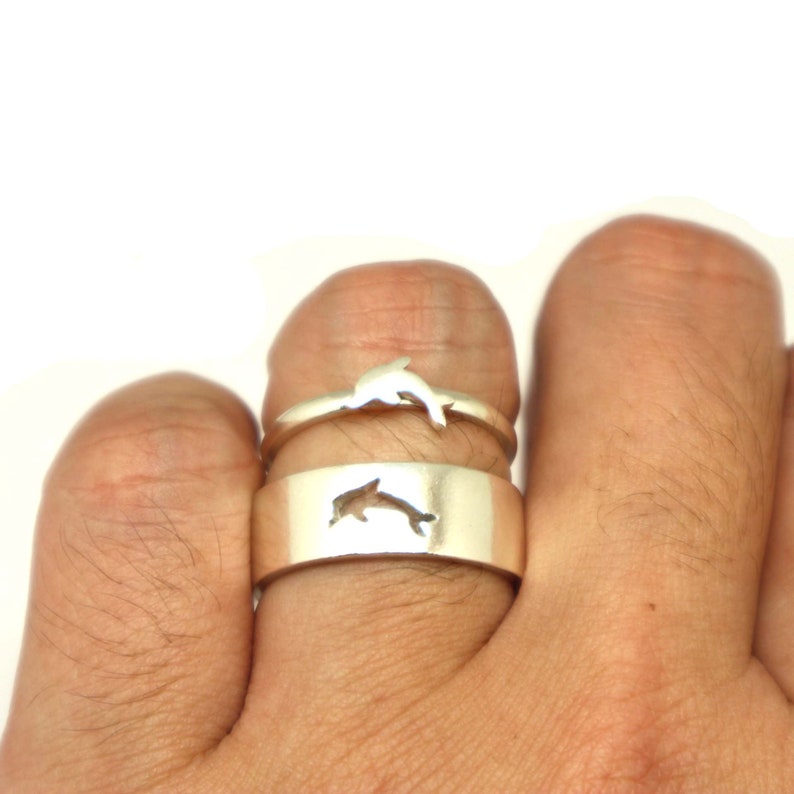May include: Two silver rings with dolphin designs. The top ring has a dolphin cutout, and the bottom ring has a solid dolphin design.