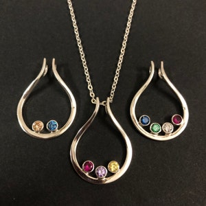 May include: A silver-toned jewelry set featuring a pendant necklace and matching earrings. Each piece has a teardrop design with colorful gemstones. The necklace has a chain, and the earrings are for pierced ears.