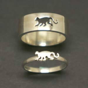Könnte beinhalten: Zwei silberne Ringe mit einem ausgeschnittenen Design eines Affen. Der größere Ring hat ein größeres Affen-Ausschnitt, während der kleinere Ring ein kleineres Affen-Ausschnitt hat.