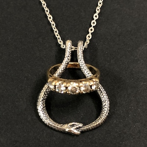 May include: A silver chain necklace with a pendant featuring a silver and gold ring with clear stones. The ring is held by a silver snake design.