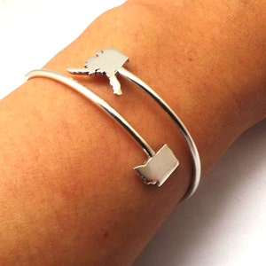May include: A silver bangle bracelet with two charms shaped like the states of Washington and Oregon.