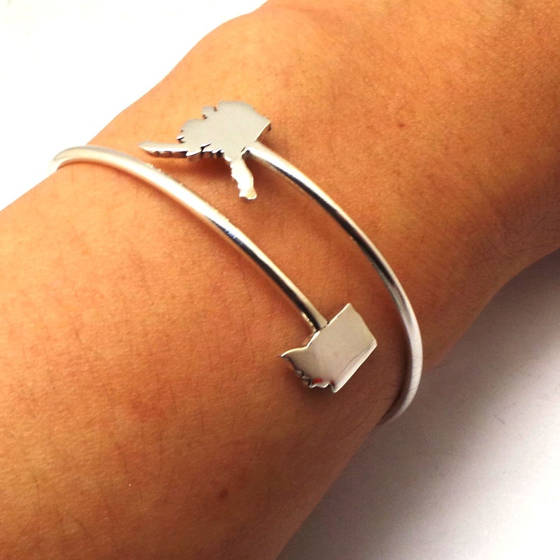 May include: A silver bangle bracelet with two charms shaped like the states of Washington and Oregon.