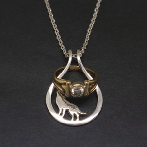 May include: A silver necklace with a silver ring and a clear gemstone. The ring is attached to a silver pendant shaped like a wolf.