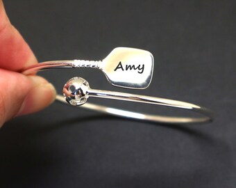 May include: Silver bracelet with a lacrosse stick charm and a lacrosse ball charm. The stick charm has the name "Amy" engraved on it.