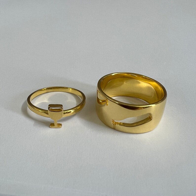 May include: Two gold rings, one with a simple design and the other with a cutout shape of a wine glass.