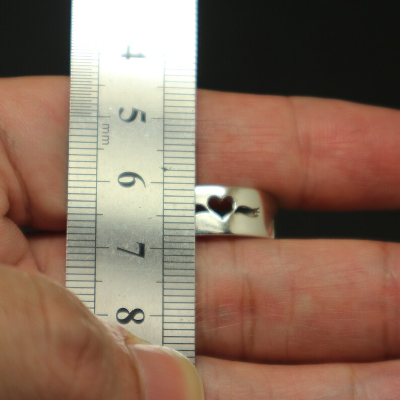 May include: A silver ring with a heart cut-out and an arrow through it. The ring is being measured with a ruler, showing it is 7 mm wide.