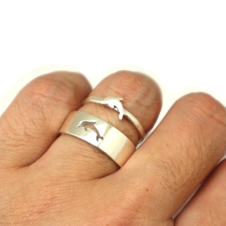 May include: Two silver rings with a dolphin design. The rings are worn on a finger.
