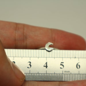 May include: A silver ring with a crescent moon design, measured on a ruler showing 4 centimeters.