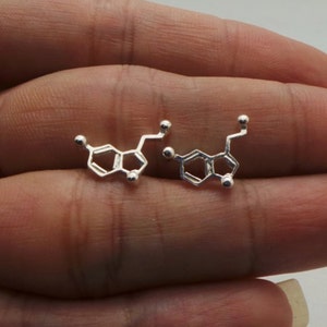 Op de afbeelding: Een paar zilveren oorbellen in de vorm van de chemische structuur van dopamine.