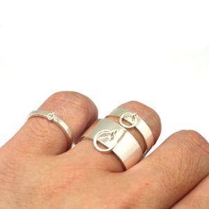 May include: Three silver rings, one with a simple design and two with a more intricate design featuring a small circle and a larger circle with a cutout shape.