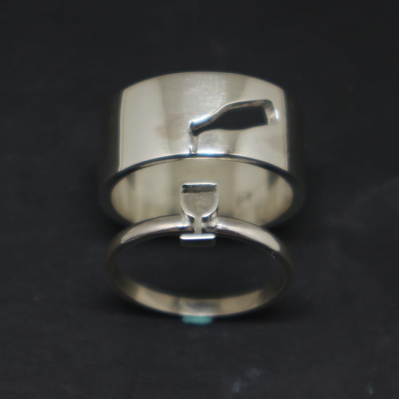 May include: Two silver wedding bands with a wine bottle and wine glass design. The bands are stacked on top of each other.