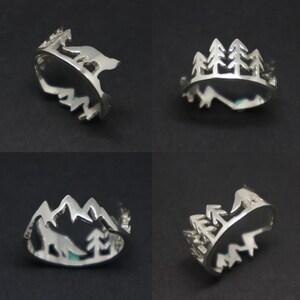 May include: Four silver rings with different nature-inspired designs. One ring features a wolf silhouette, another has a mountain range, and two rings have a silhouette of a group of trees.