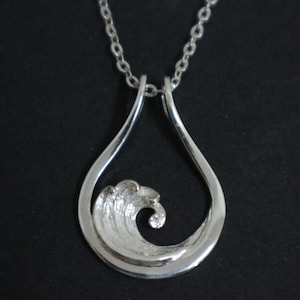 May include: A silver pendant necklace with a wave design inside a teardrop shape. The wave is textured, and the necklace has a fine chain. The pendant is a bright, reflective silver.