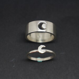 May include: Two silver rings with a crescent moon design. The larger ring has a cut-out crescent moon, while the smaller ring has a solid crescent moon.