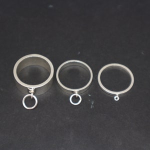 May include: Three silver rings with a circular design. The largest ring has a small circular charm attached to it.