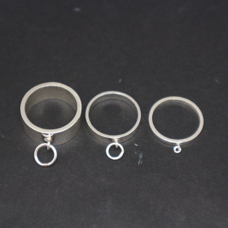 May include: Three silver rings with a circular design. The largest ring has a small circular charm attached to it.