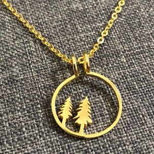 Puede incluir: Collar de oro con un colgante circular que presenta dos pinos estilizados. El colgante es hueco y los árboles están recortados en el metal.