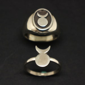 May include: Two silver rings with a stylized crescent moon and circle design. The top ring has a black enamel background.