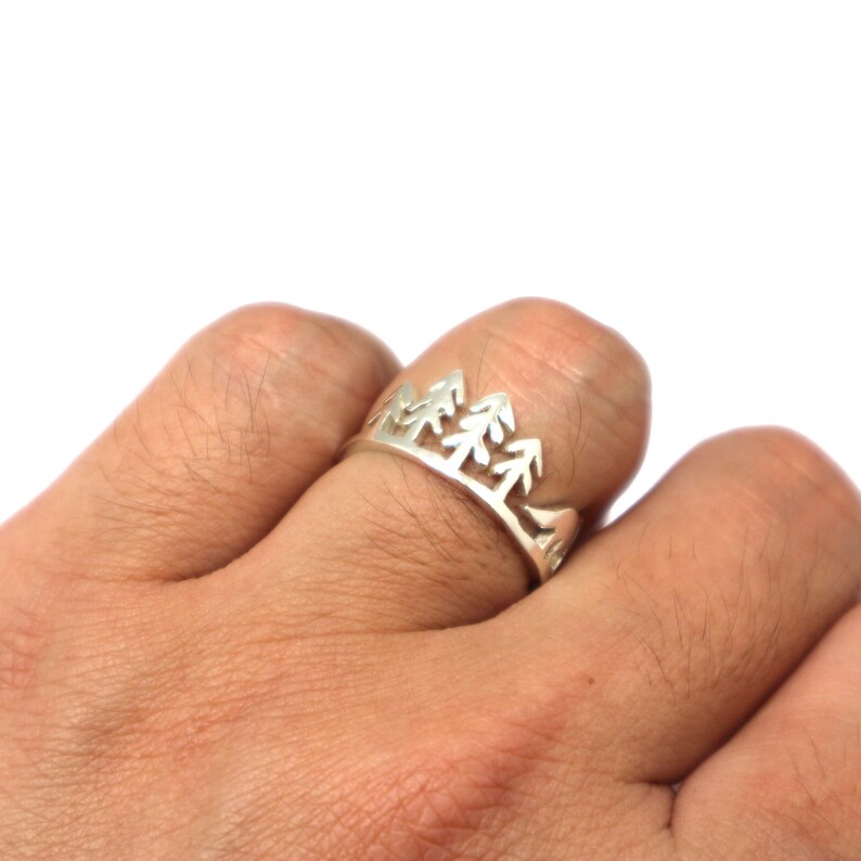 May include: A silver ring featuring a cut-out design of three pine trees.