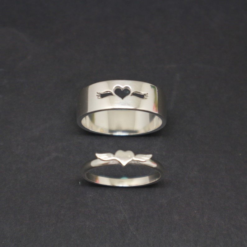 May include: Two silver rings with heart cutouts. The larger ring has a heart with an arrow through it. The smaller ring has a heart with wings.