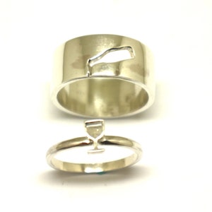 May include: Two silver rings, one with a cutout of a wine glass and the other with a wine bottle cutout.