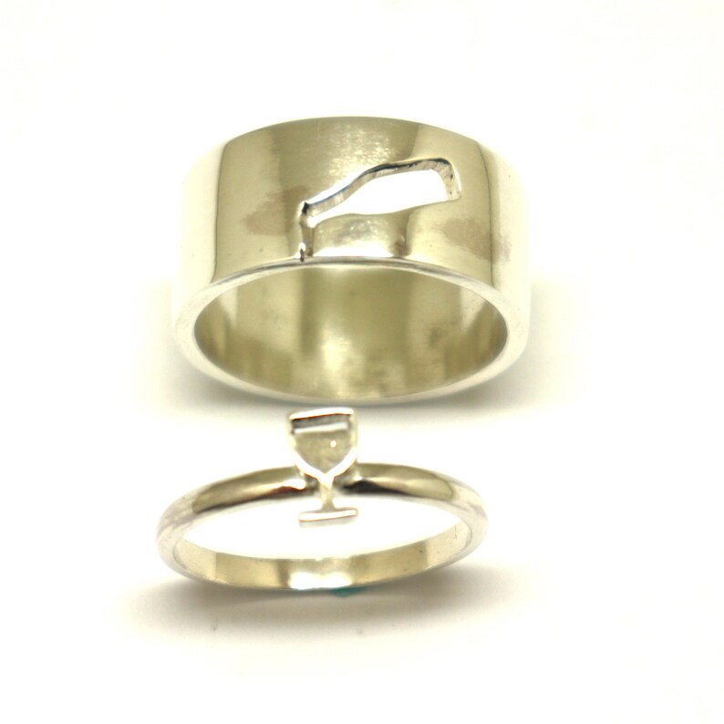 May include: Two silver rings, one with a cutout of a wine glass and the other with a wine bottle cutout.