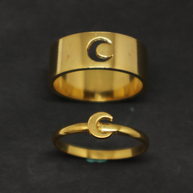 May include: Two gold rings with a crescent moon design. The larger ring has a cutout crescent moon, while the smaller ring has a solid crescent moon.