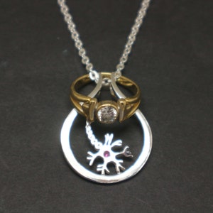 May include: A silver necklace with a silver ring and a silver neuron pendant. The ring has a clear stone in the center. The neuron pendant has a pink stone in the center.