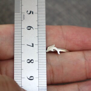 May include: A silver dolphin ring with a size 7 measurement shown on a ruler.