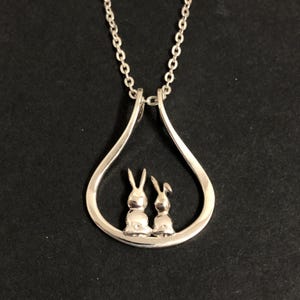 May include: A silver necklace with a teardrop-shaped pendant featuring two small rabbit silhouettes inside.