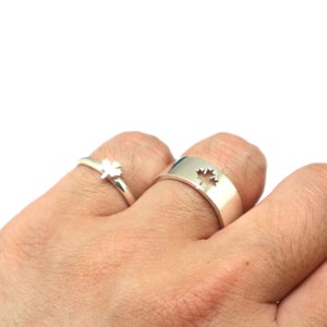May include: Two silver rings, one a band with a maple leaf cutout, the other a delicate ring with a maple leaf design. The rings are displayed on a hand against a white background. The rings are likely made of sterling silver.