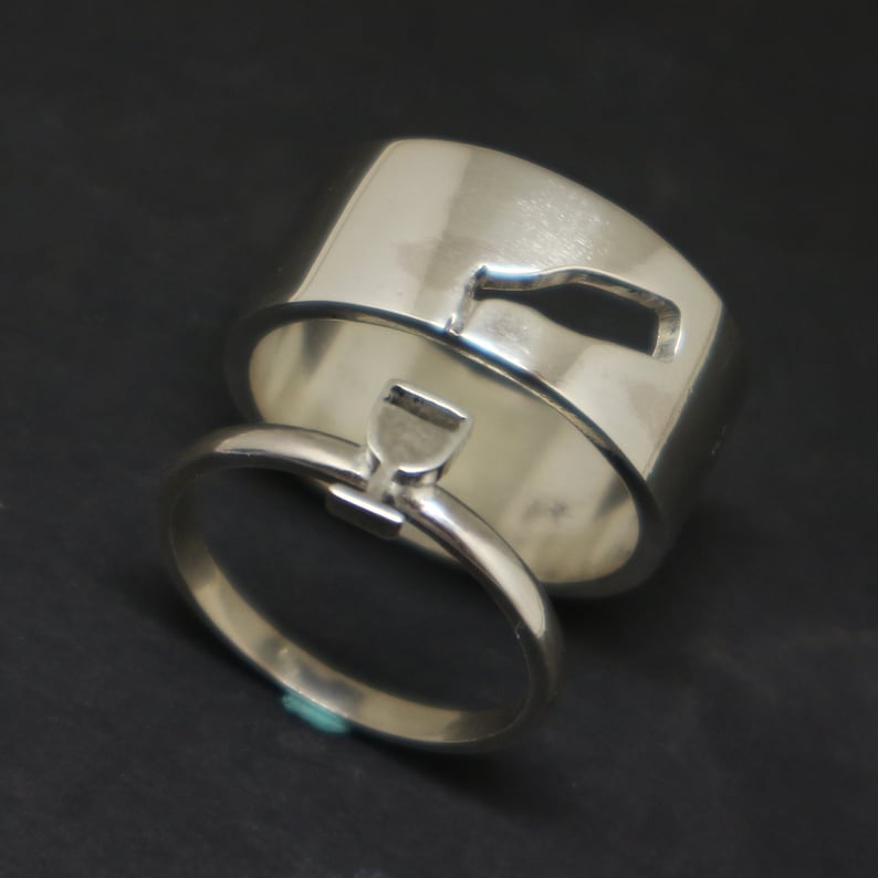 May include: Two silver rings with a bottle and a glass design. The rings are interlocked.