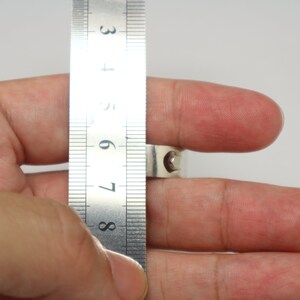 May include: A silver ring being measured with a ruler. The ruler shows the ring is between 7 and 8 centimeters in diameter.