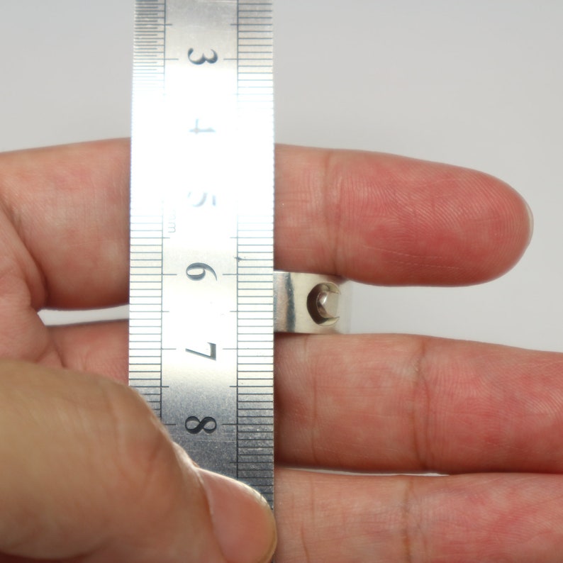 May include: A silver ring being measured with a ruler. The ruler shows the ring is between 7 and 8 centimeters in diameter.