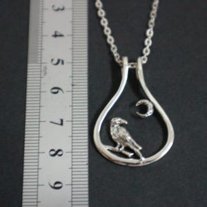 May include: Silver pendant necklace with a bird on a branch inside a teardrop frame, and a crescent moon. The necklace has a fine chain. The pendant is approximately 4 cm in length.