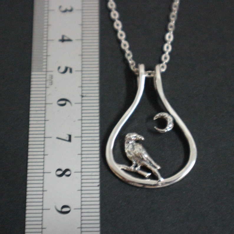May include: Silver pendant necklace with a bird on a branch inside a teardrop frame, and a crescent moon. The necklace has a fine chain. The pendant is approximately 4 cm in length.