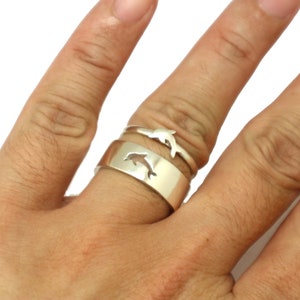 May include: Two silver rings with dolphin designs. The larger ring has a solid band with a cutout dolphin shape. The smaller ring has a thin band with a dolphin jumping out of the water.