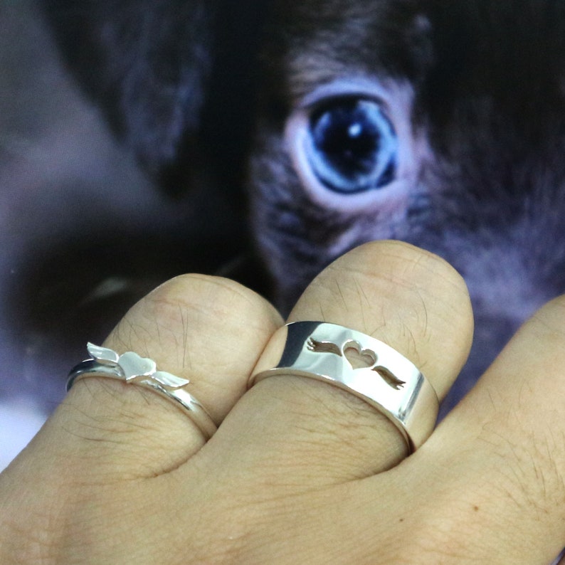 May include: Two silver rings with a heart design. One ring has a heart with wings and the other has a heart with an arrow through it.