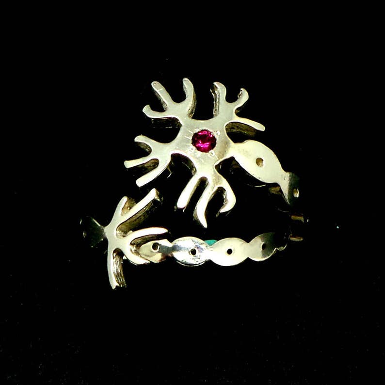 May include: A silver ring with a red gemstone in the center, shaped like a stylized neuron.