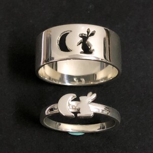 Puede incluir: Dos anillos de plata con un diseño de luna creciente y conejo. El anillo superior es más ancho y el anillo inferior es más delgado.