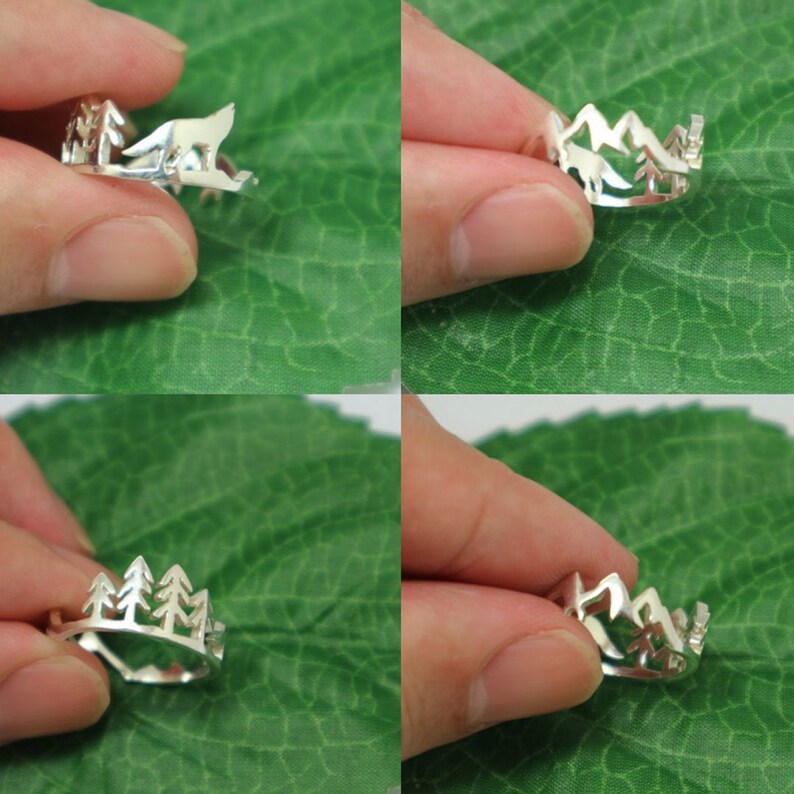 May include: Silver ring featuring a cut-out design of a mountain range and trees. The ring is displayed on a finger against a green leafy backdrop.